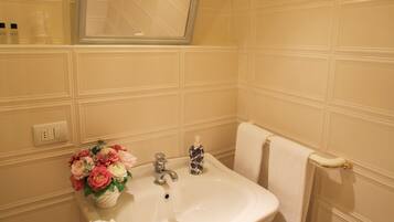 Une salle de bain avec un lavabo blanc, un miroir, un luminaire et une poubelle.