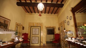 A dining area with wooden beams, a chandelier, red chairs, a buffet table with food, and a wall with decorative plates. - B&B Le Aquile (Siena)