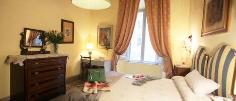 A bedroom with a bed, dresser, desk, lamp, and a window with curtains.