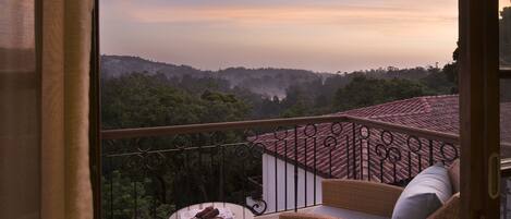 A balcony with wicker furniture, a glass table, and a view of a hilly landscape.