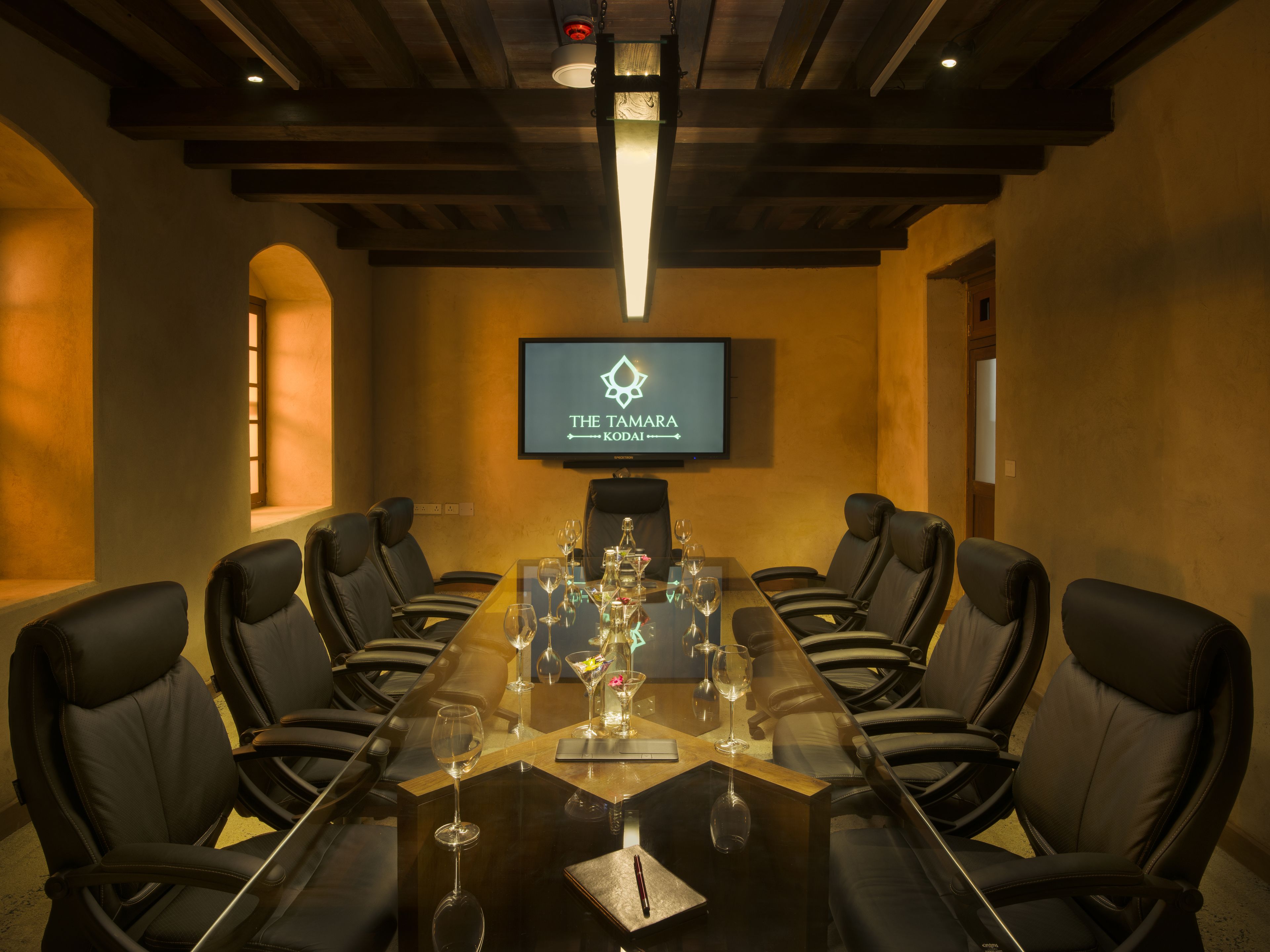 A conference room with a long table, black leather chairs, and a screen displaying "The Tamar Kodaï".
