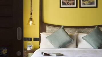 A hotel room with a bed, two pillows, a nightstand with a lamp, and two framed pictures on the wall.
