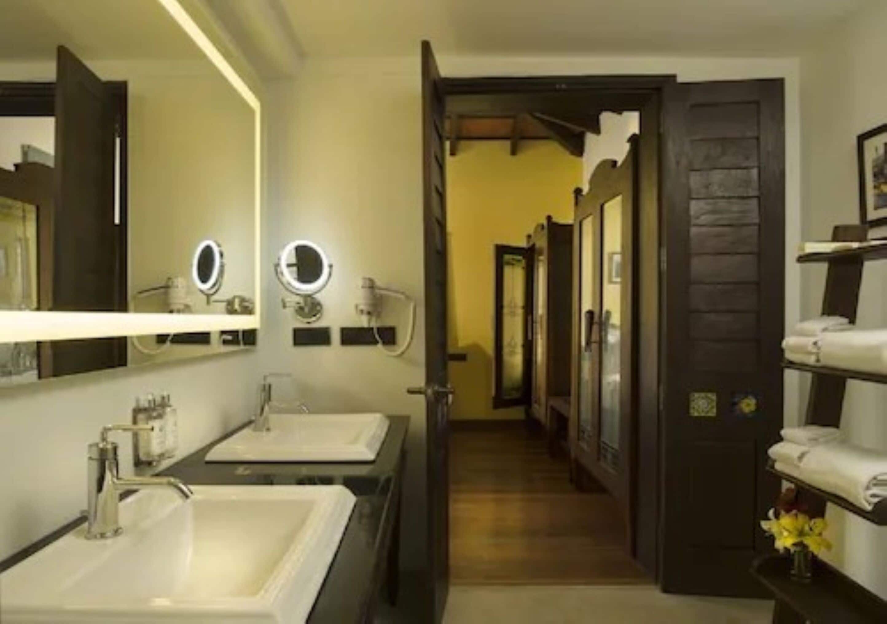 A modern bathroom with two sinks, a mirror with a light, and a wooden door.