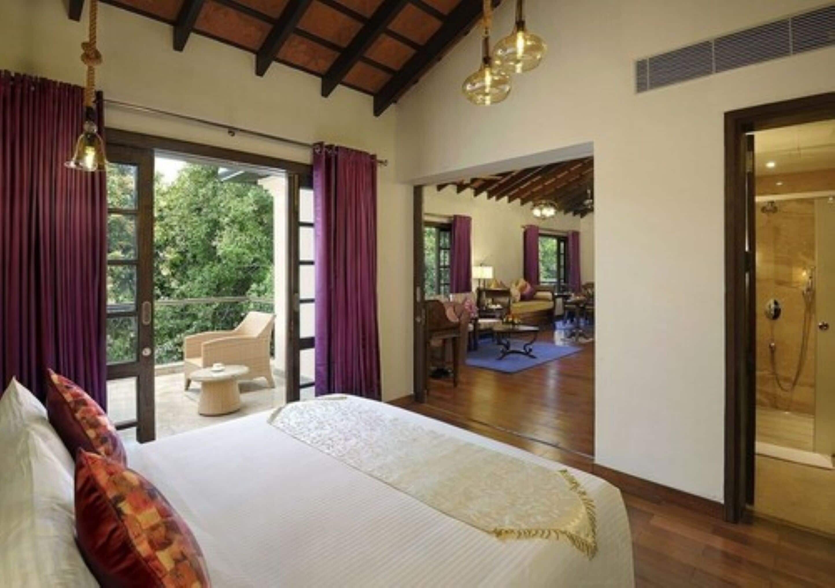 Habitación de hotel con una cama grande, un balcón con cortinas, una zona de comedor y una ducha.