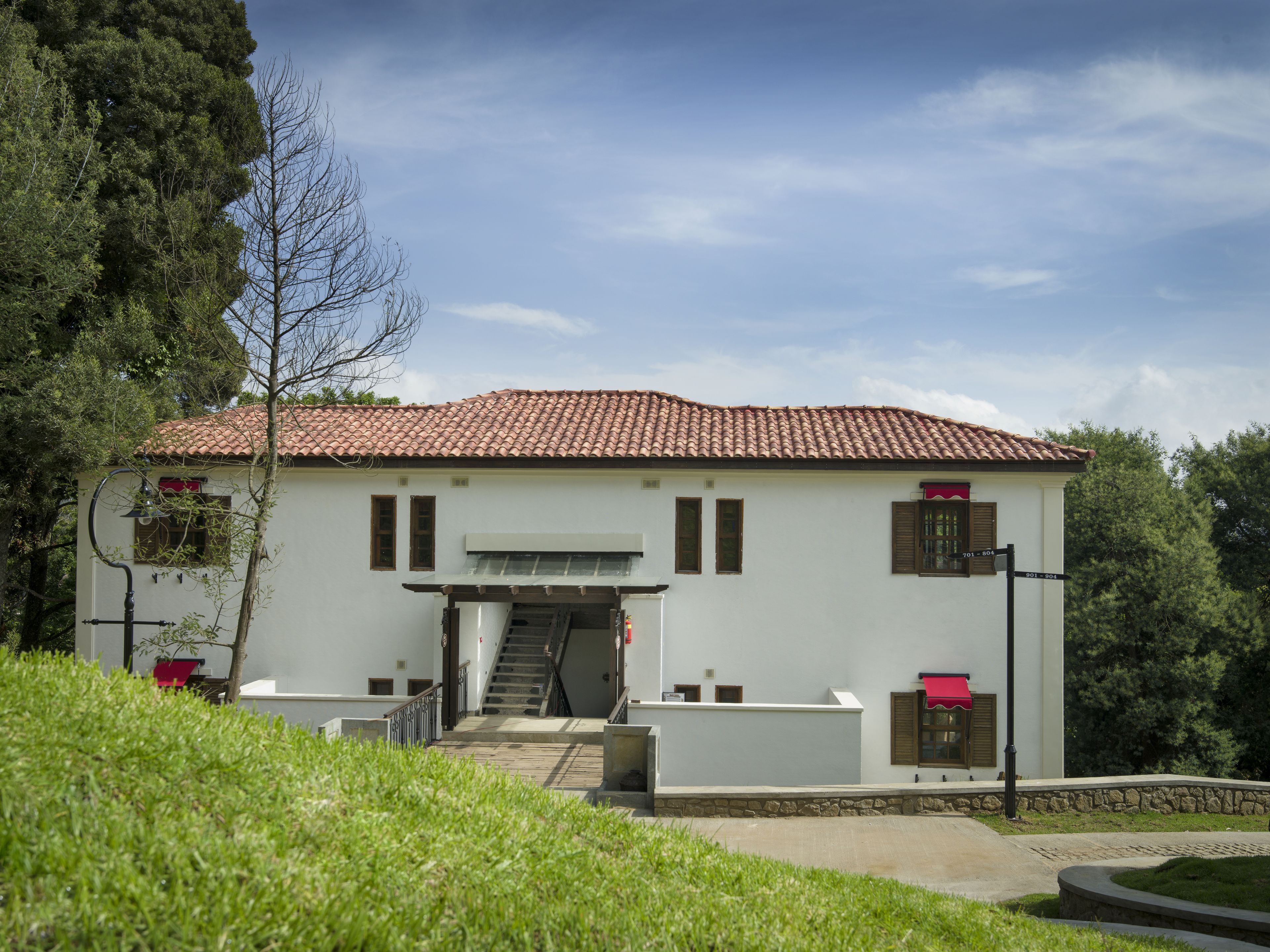 A two-story building with a tiled roof, a staircase leading to the entrance, and a small garden area in front.