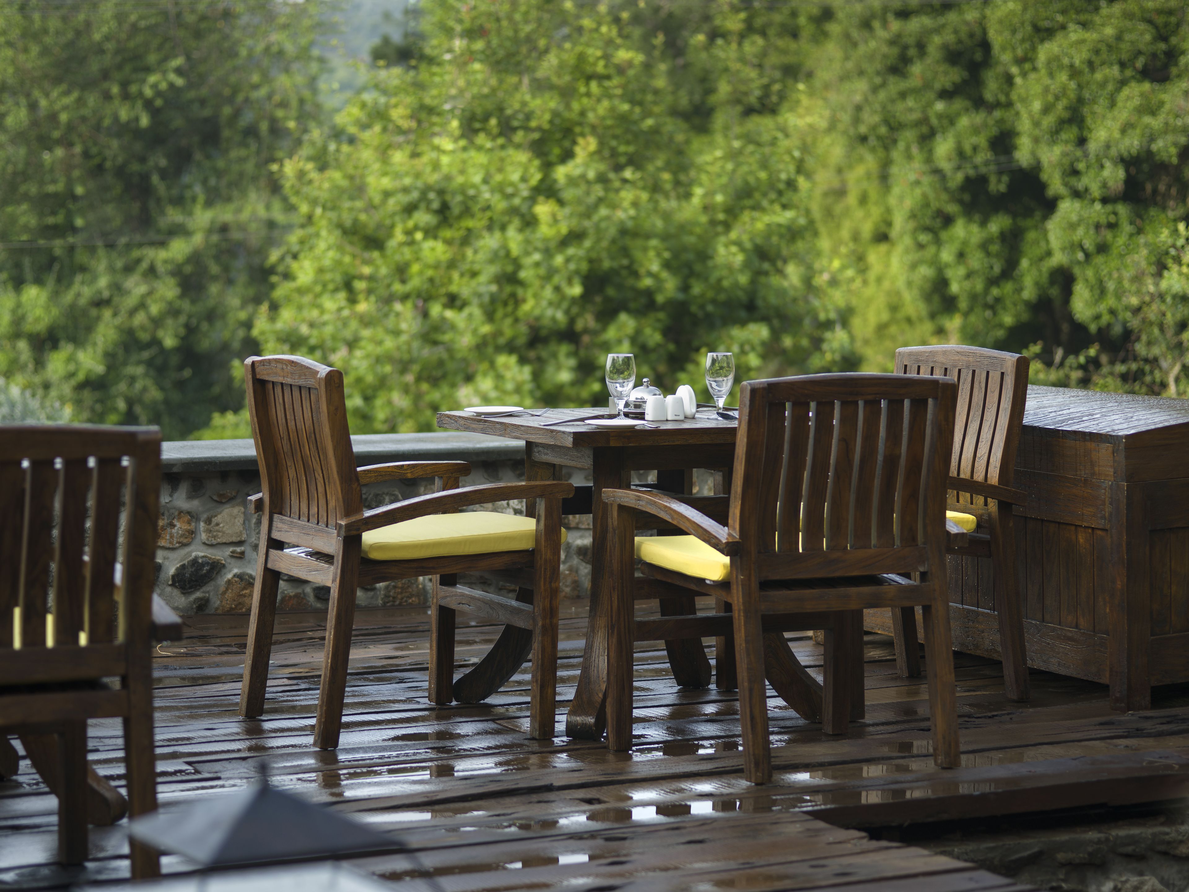An outdoor wooden deck with a table and chairs, surrounded by lush greenery.