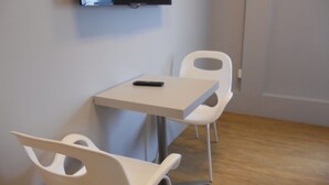 Una habitación pequeña con una mesa, dos sillas, un televisor montado en la pared y piso de madera.