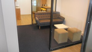 Un espacio de oficina moderno con un sofá gris, dos otomanas beige y una pequeña mesa blanca.