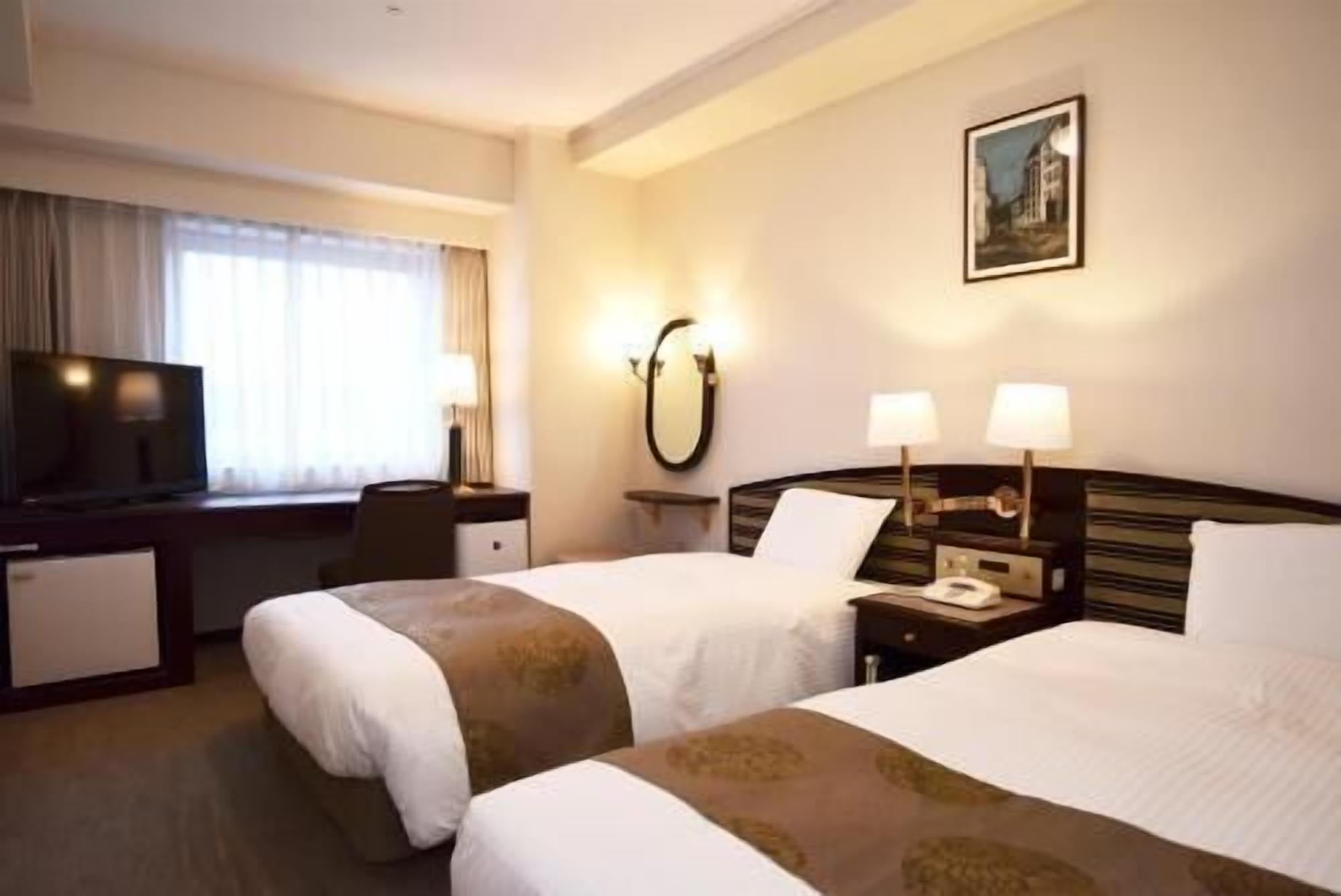 Une chambre d’hôtel avec deux lits, un bureau avec une télévision, un miroir et un tableau au mur.