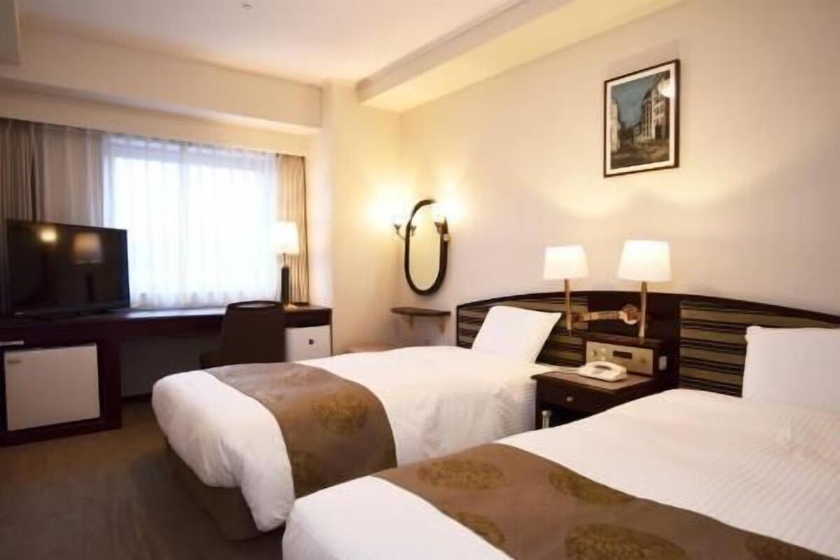 A hotel room with two beds, a desk with a television, a mirror, and a painting on the wall.