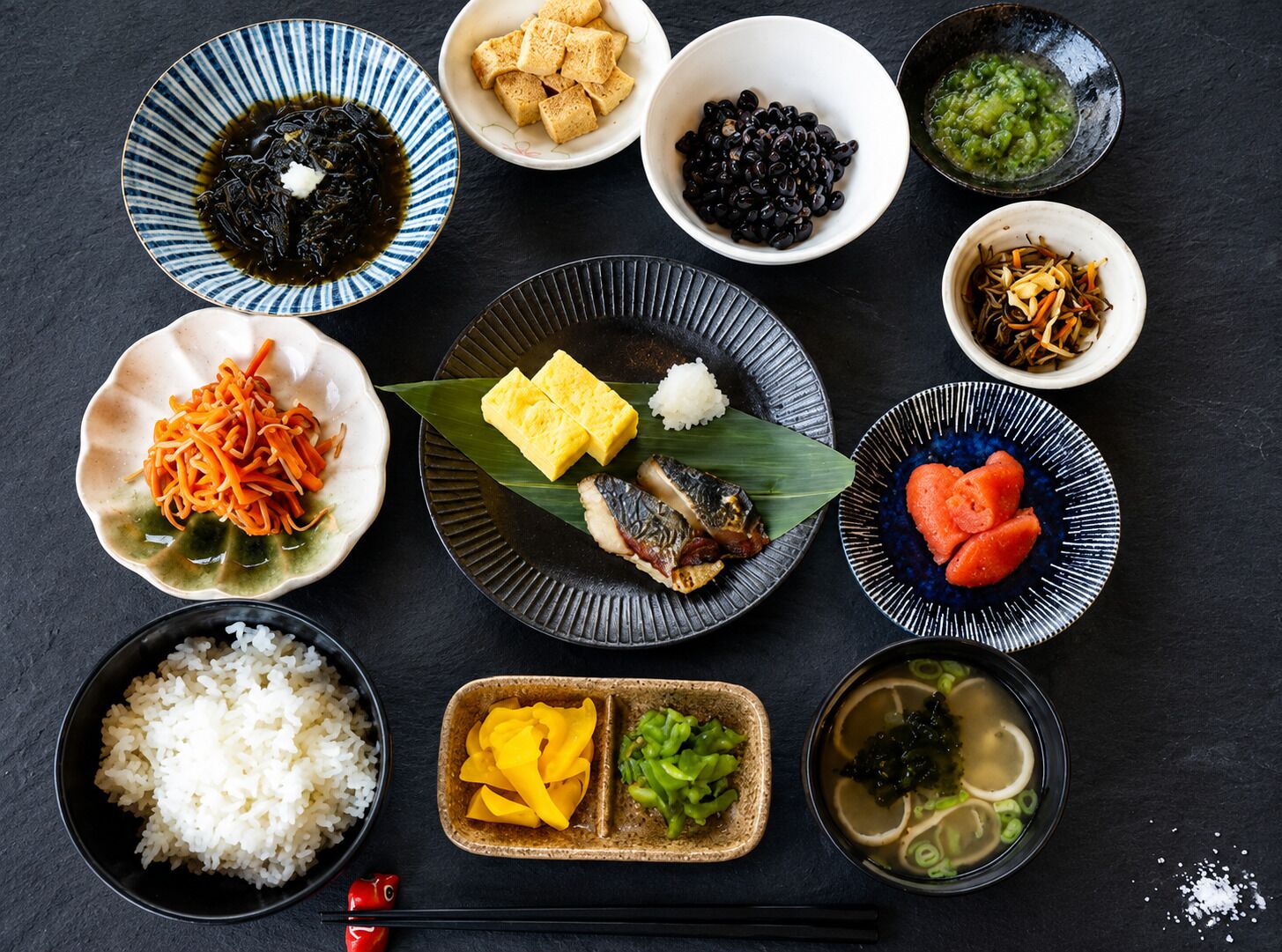 A variety of Japanese dishes arranged on a dark surface.