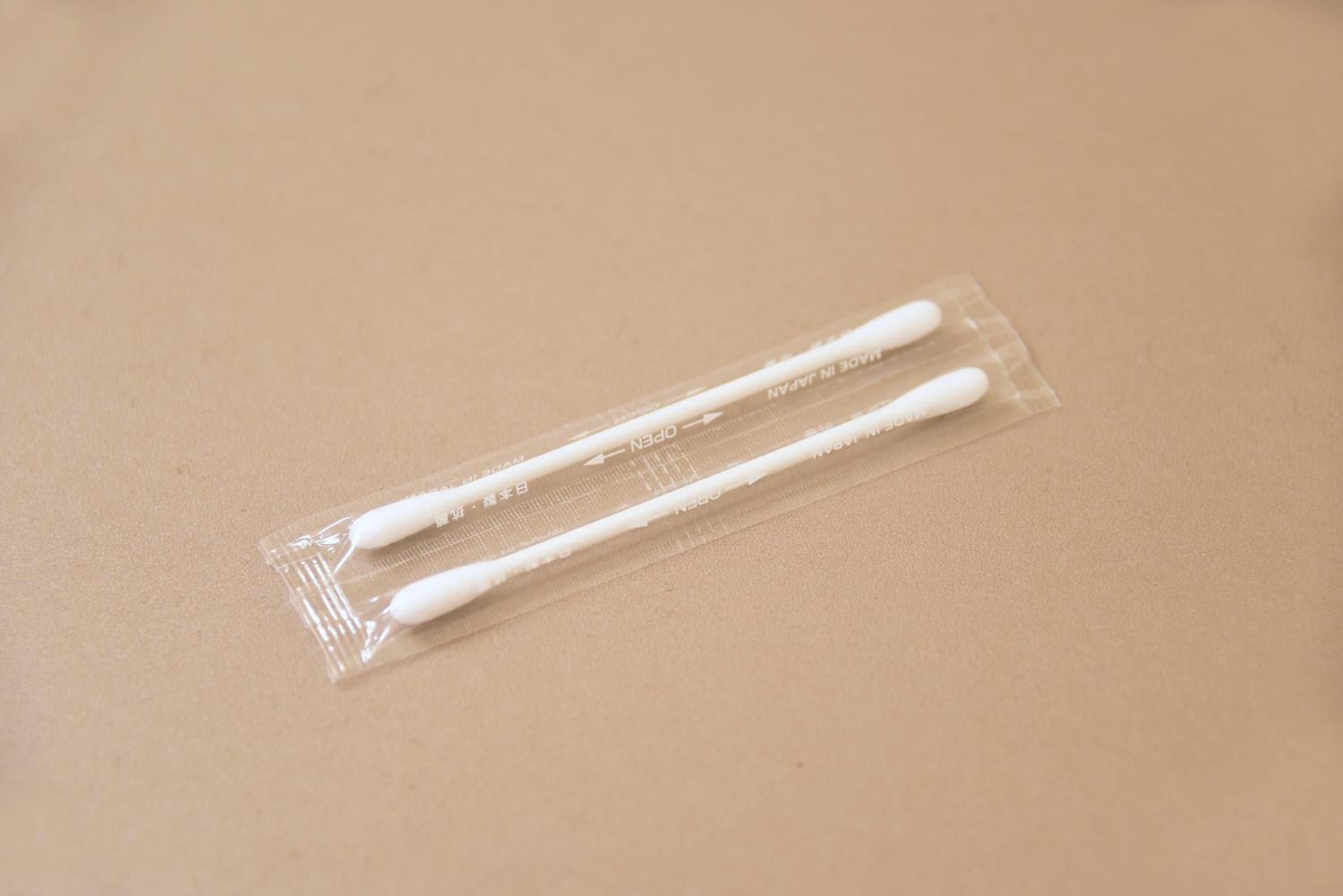 Un emballage transparent en plastique contenant deux cotons-tiges blancs sur une surface beige.