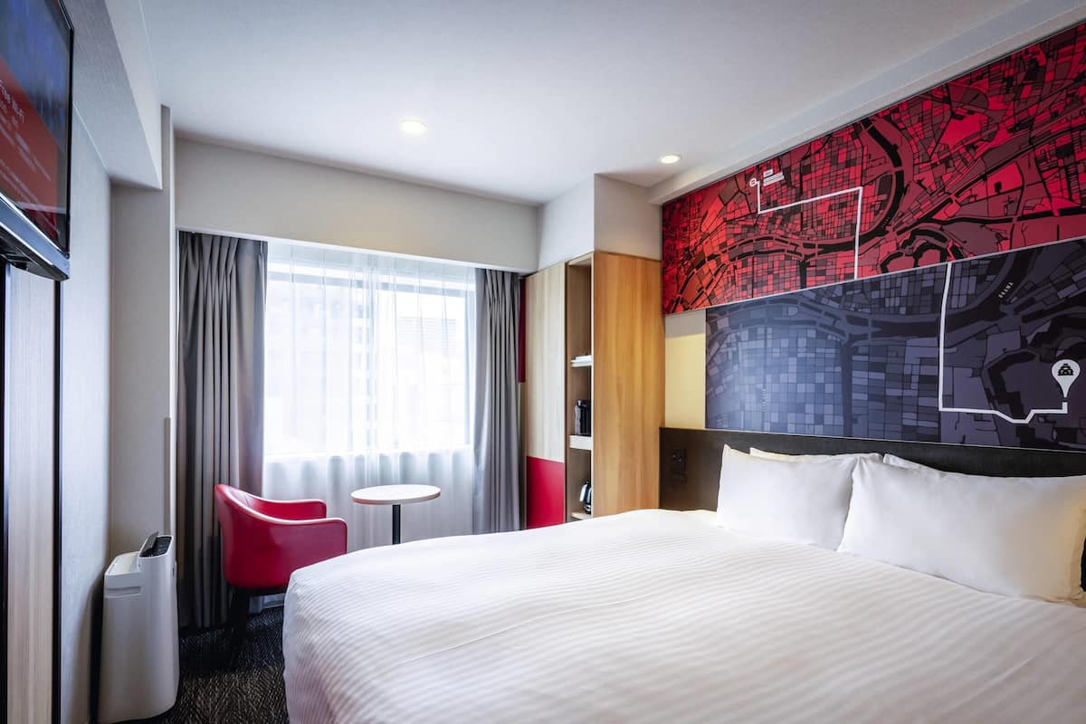 Habitación de hotel con una cama grande, una mesita pequeña, una silla roja y un mapa en la pared.
