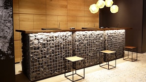 Un área de recepción con mostrador de madera, pared de piedra y tres taburetes.