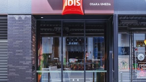 El exterior de un hotel ibis con un diseño moderno, que presenta un llamativo logotipo rojo y el nombre 'OSAKA UMEDA'.