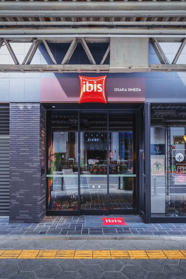 The exterior of an ibis hotel with a modern design, featuring a prominent red logo and the name 'OSAKA UMEDA'. - ibis Osaka Umeda (Osaka)