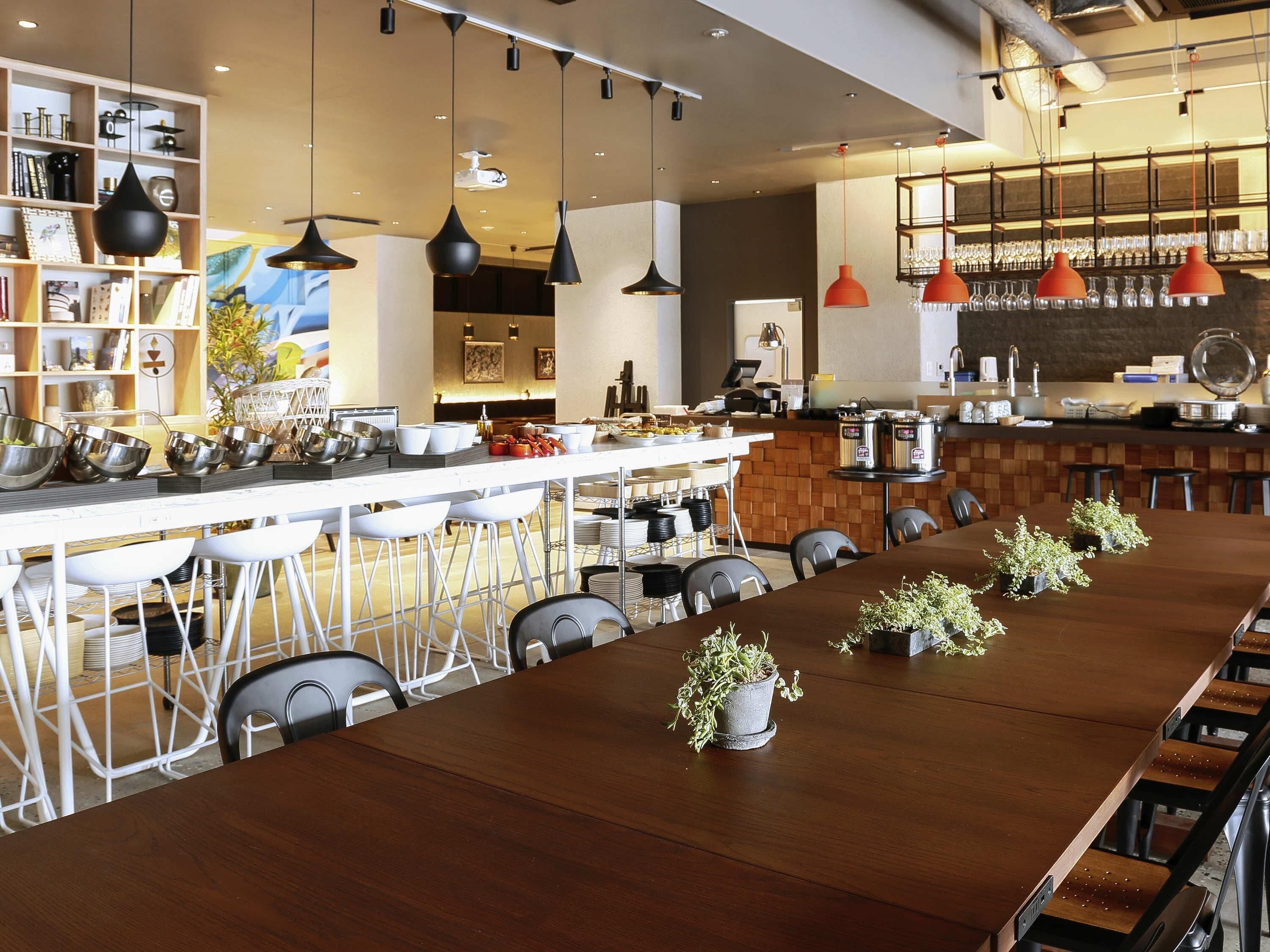 Un restaurante moderno con una larga mesa de madera, asientos de bar e iluminación colgante.