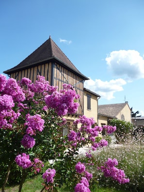 A traditional half-timbered building with a steeply pitched roof, surrounded by lush purple flowering bushes. - Les Sureaux (Le Pizou)