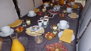 A dining table set with various dishes, including fruits, pastries, and condiments, in a room with chairs and a window. - Les Sureaux (Le Pizou)