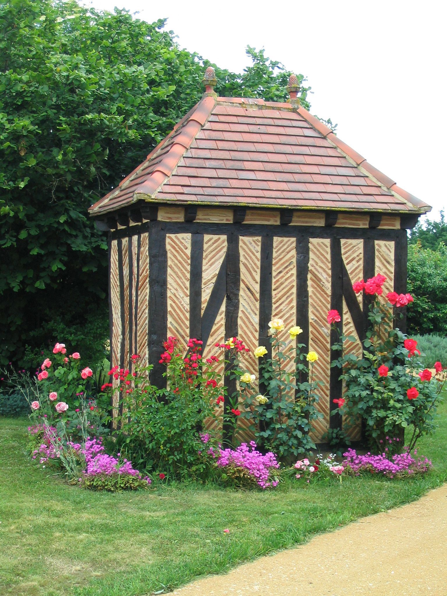 Ein Gartenpavillon mit Ziegeldach, umgeben von verschiedenen blühenden Pflanzen.