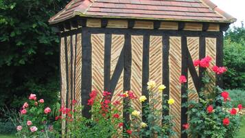 Ein Gartenpavillon mit Ziegeldach, umgeben von verschiedenen blühenden Pflanzen.