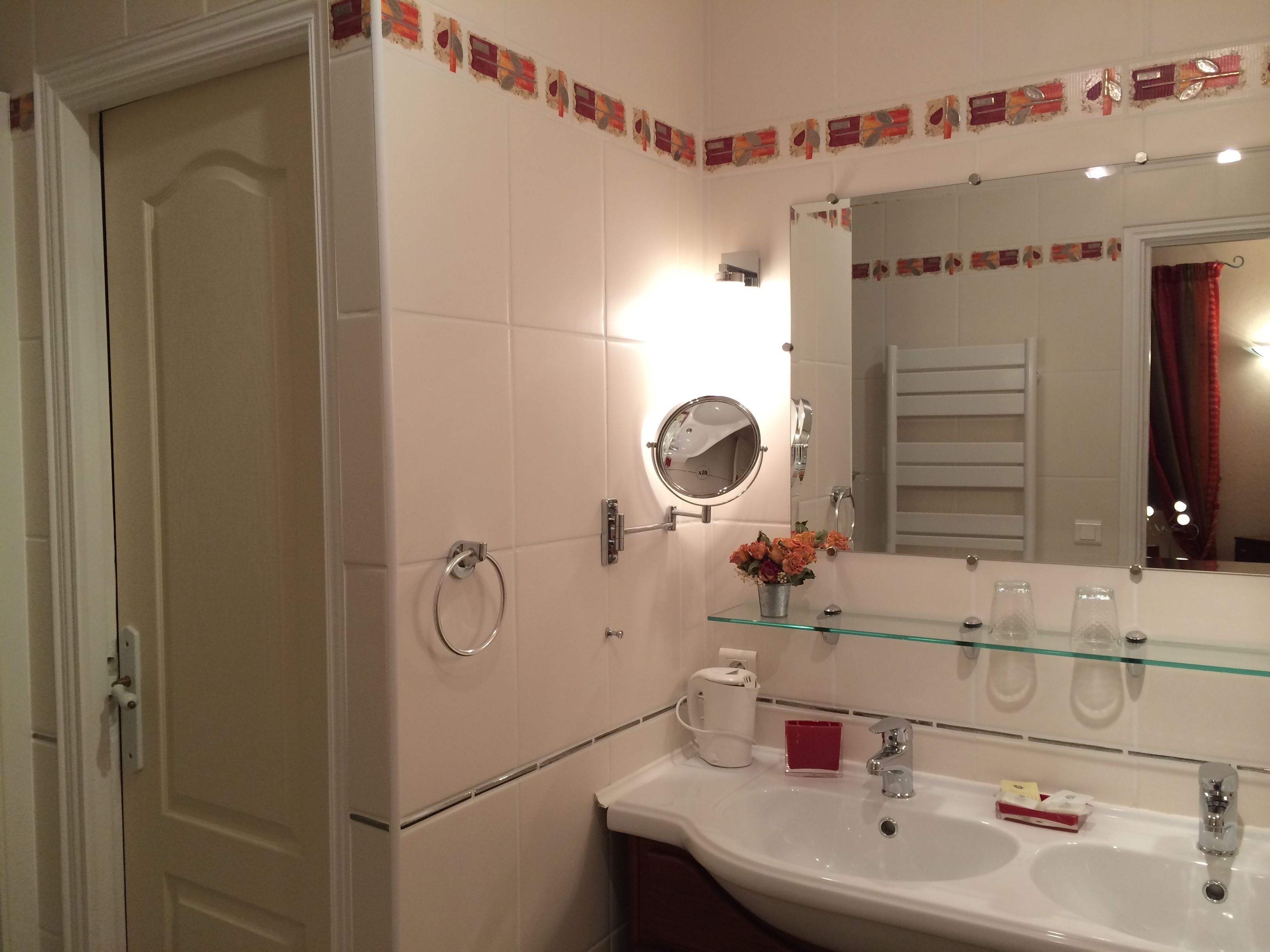 Un baño con lavamanos blanco, repisa de vidrio, espejo redondo y toallero.