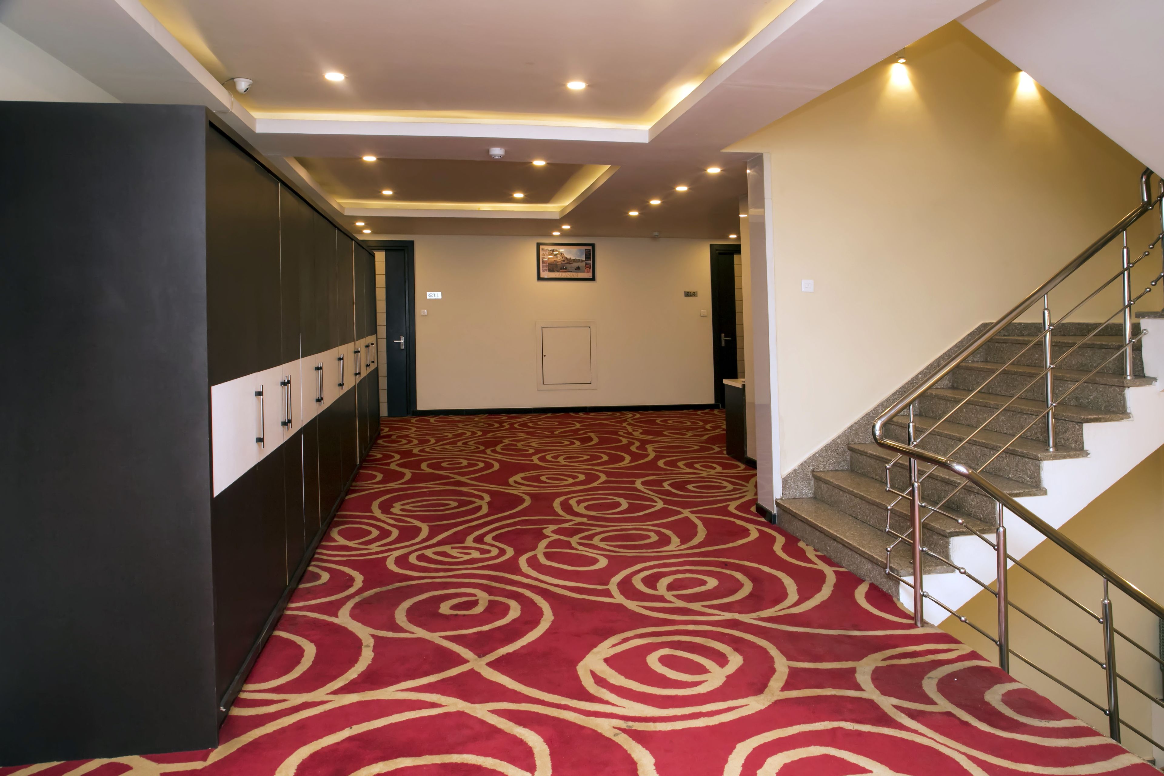 Un couloir avec un tapis rouge, un escalier et une caméra de surveillance fixée au plafond.
