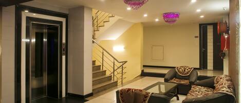 A lobby with a staircase, elevator, and seating area with a patterned throw on the sofa.