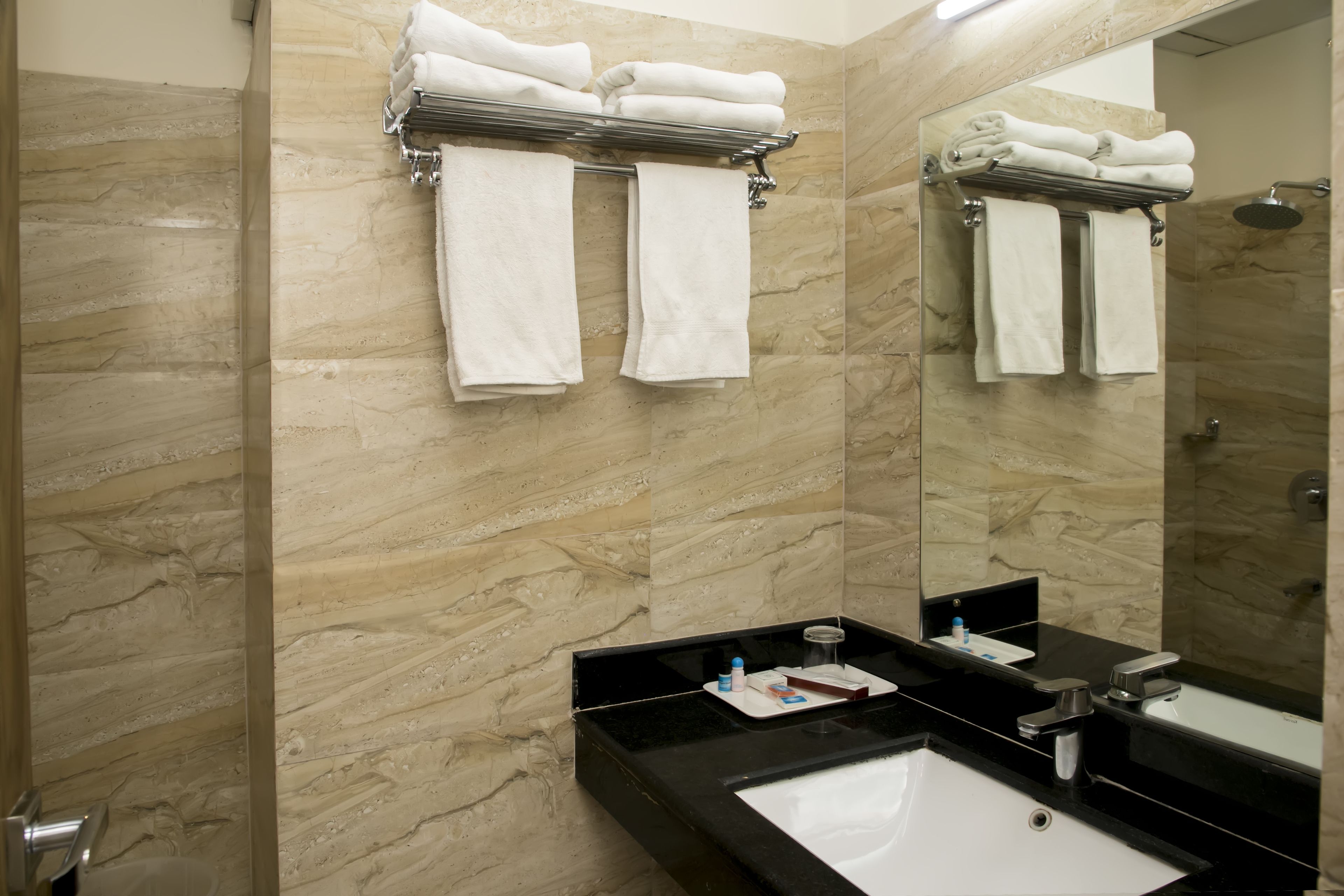 A bathroom with a marble wall, a black sink, and a mirror reflecting a towel rack with folded towels.
