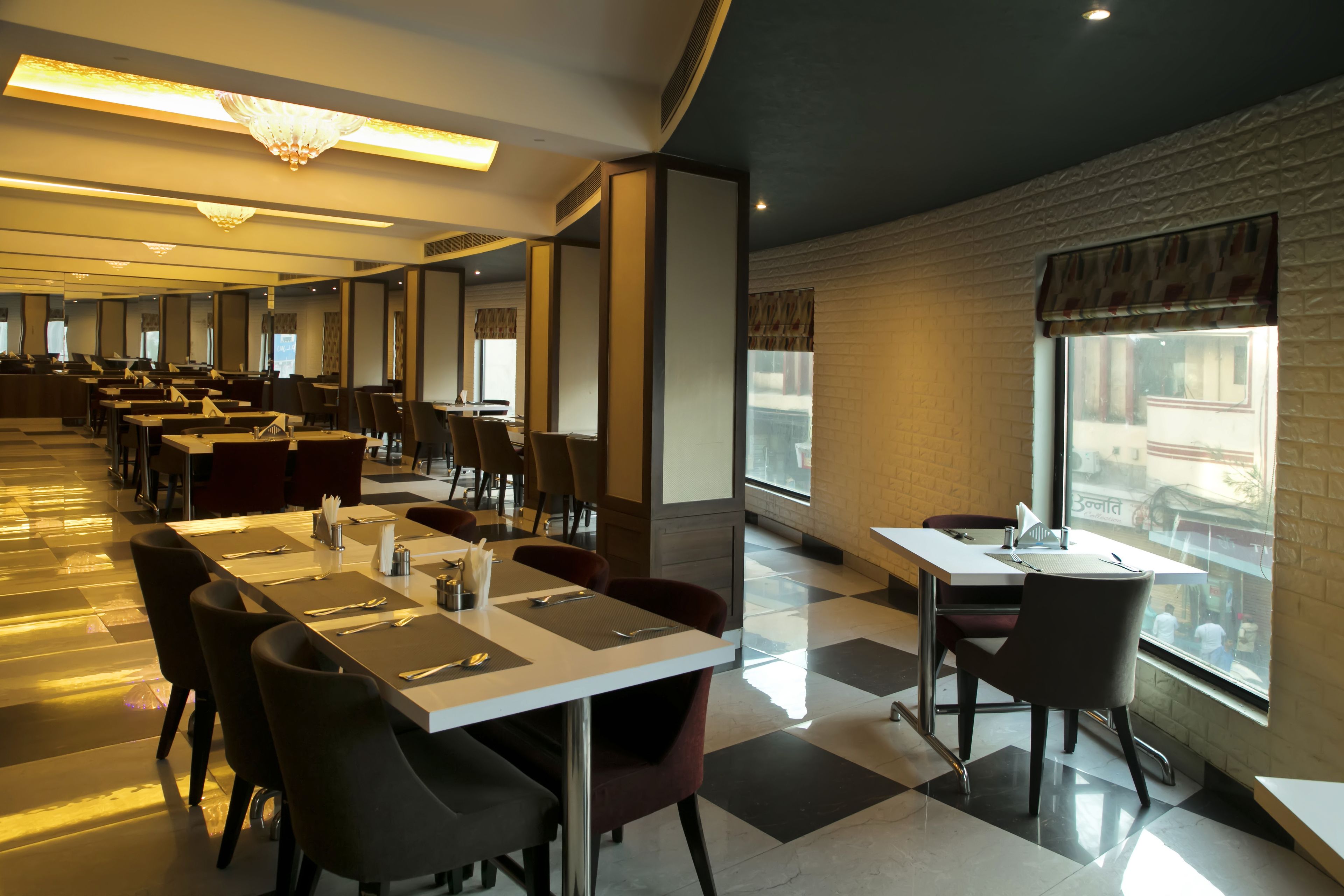A modern restaurant with long tables and chairs, large windows, and a chandelier.