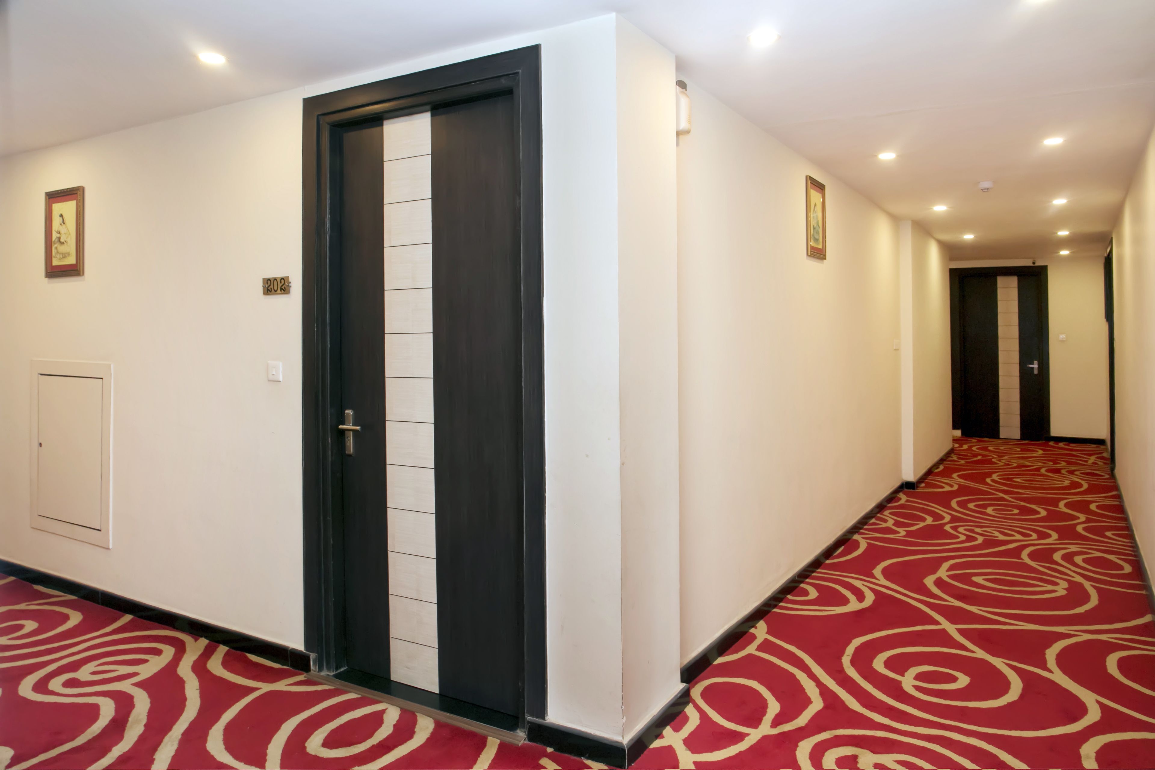 Ein Hotelgang mit rotem Teppich, einer dunklen Holztür und weißen Wänden.