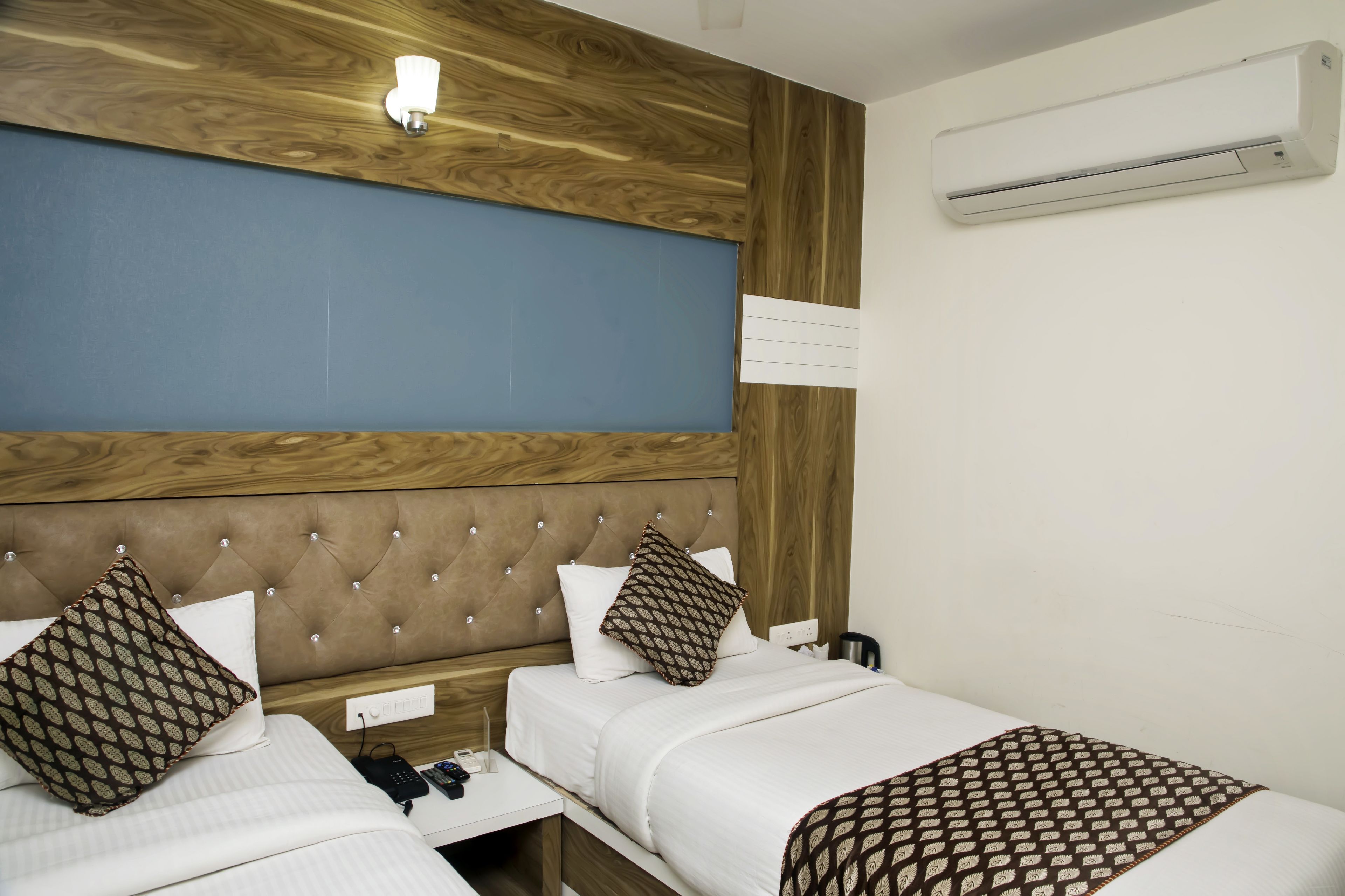 Hotelkamer met twee bedden, een houten hoofdbord, een wandairconditioner en een nachtkastje met telefoon en afstandsbediening.