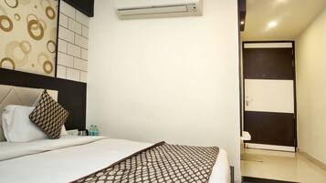Habitación de hotel con una cama, un plaid estampado, un equipo de aire acondicionado, un baño con espejo y puerta, y una pared con diseño circular.