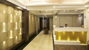 Zona de recepción de un hotel, con mostrador, sala de espera y un pasillo con pared estampada y suelo de madera.