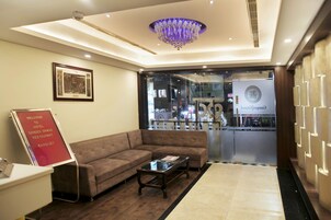 A hotel lobby with a reception desk, a brown sofa, a glass coffee table, and a chandelier.