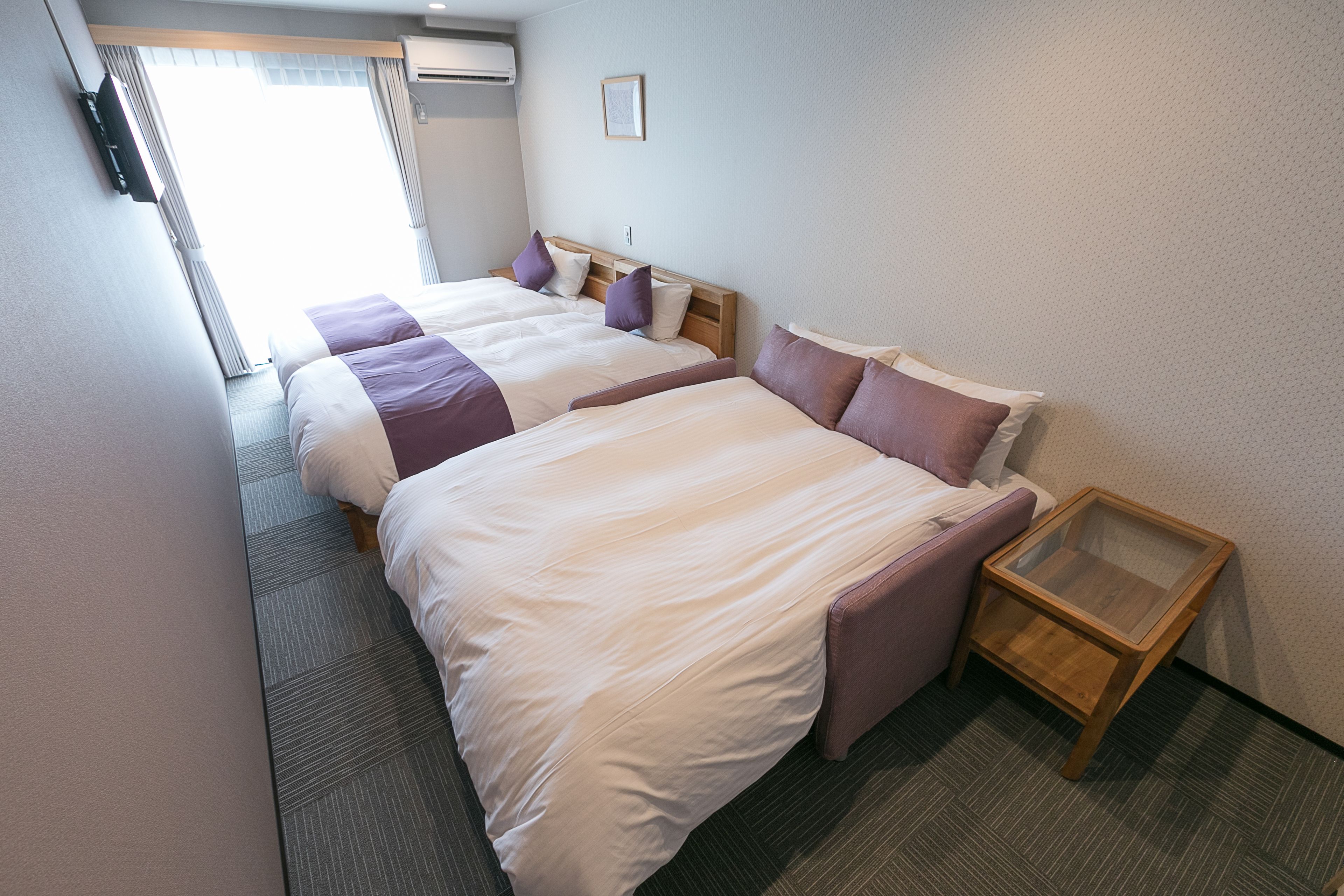 A hotel room with two beds, a wooden nightstand, and a window with curtains.