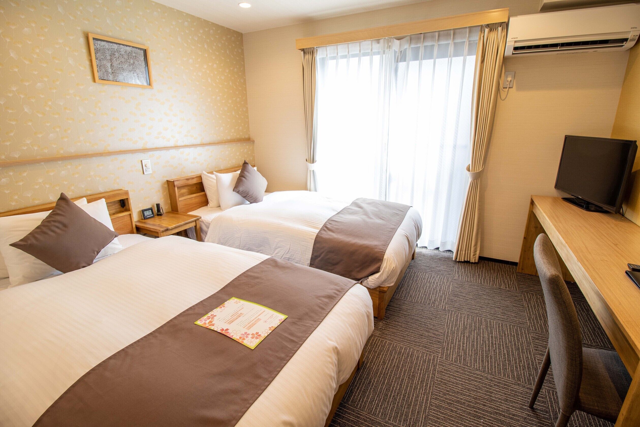 Une chambre d’hôtel avec deux lits, un bureau, une télévision et une fenêtre avec des rideaux.