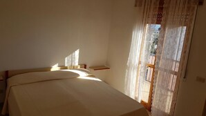 Quarto com cama, janela com cortinas leves e vista para o exterior.