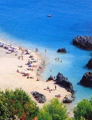 A beach with people sunbathing and swimming, surrounded by rocks and greenery. - Parco Degli Emiri (Scalea)
