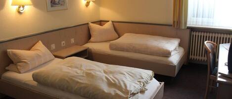 Habitación de hotel con dos camas individuales, una mesita pequeña, dos lámparas de pared y un ventanal con cortinas.