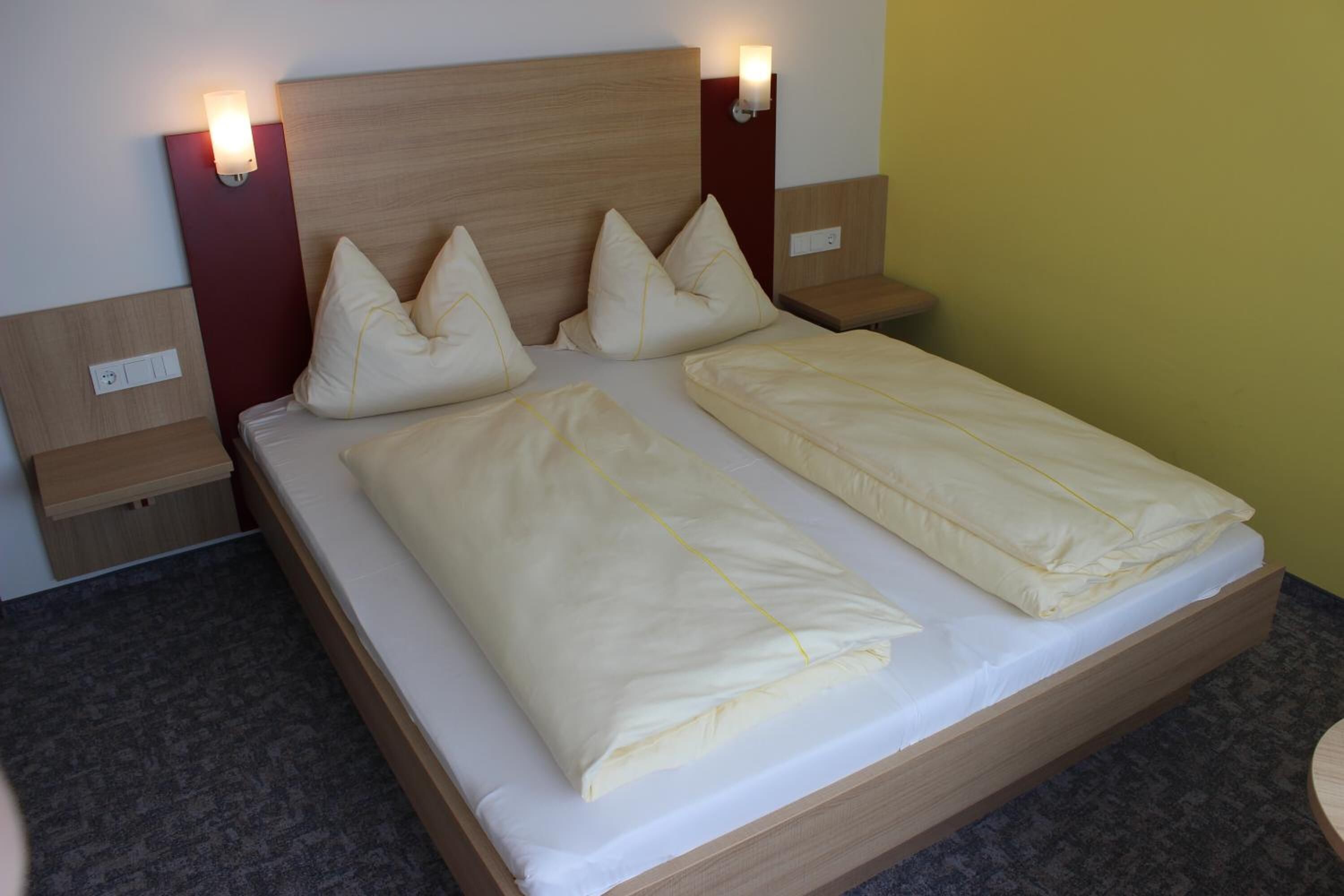 Una cama doble con dos almohadas, cabecera de madera, mesitas de noche con lámparas y suelo cubierto de alfombra.