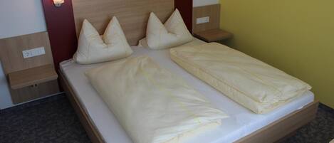 Una cama doble con dos almohadas, cabecera de madera, mesitas de noche con lámparas y suelo cubierto de alfombra.