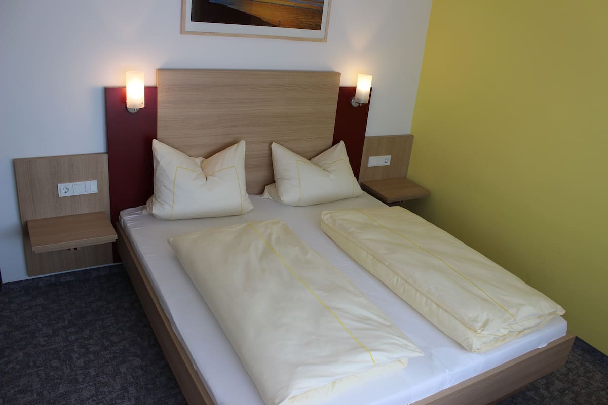 A double bed with two pillows, a wooden headboard, and bedside tables with wall-mounted lights.