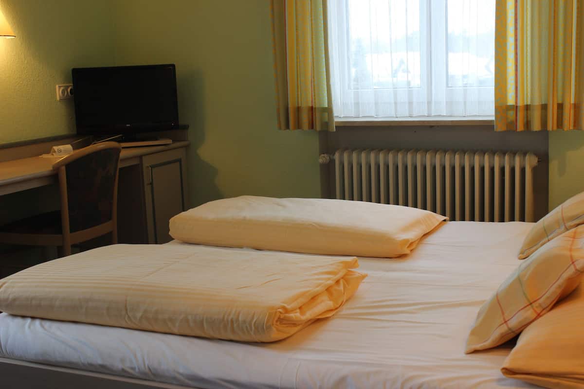 A hotel room with a bed, a desk with a television, and a window with curtains.