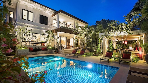 Uma casa de dois andares com piscina, área de estar externa e vegetação exuberante.