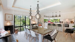 Uma cozinha moderna com ilha central, iluminação pendente e vista para o verde lá fora.