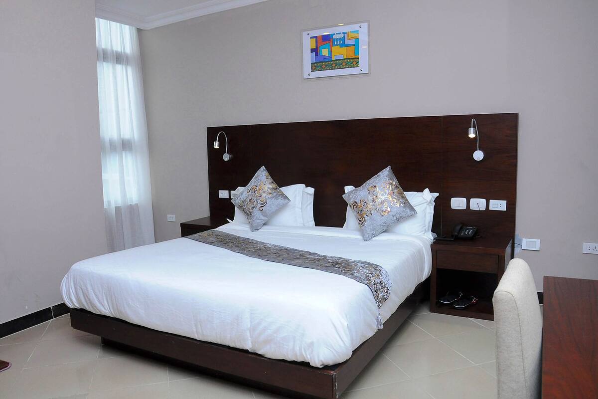 A neatly made bed with a wooden headboard, a bedside table with a phone, and a pair of shoes on the floor.
