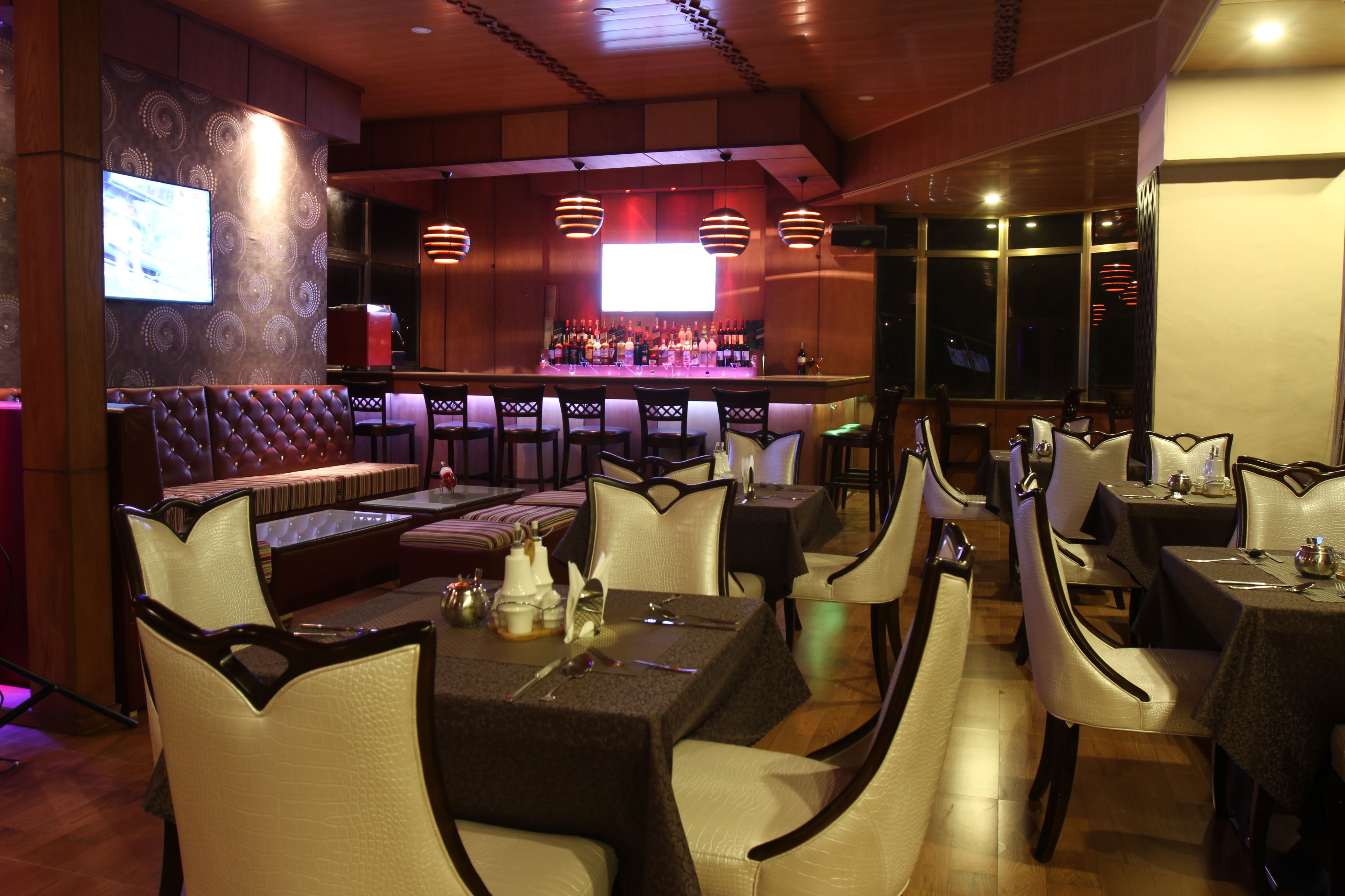 A restaurant with a bar area, cushioned seating, and tables with chairs.
