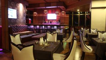 A restaurant with a bar area, cushioned seating, and tables with chairs.