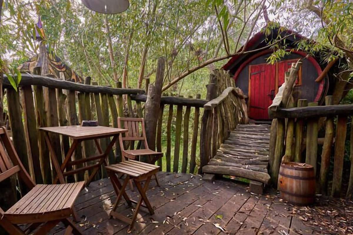 A wooden deck with two chairs and a table, surrounded by a rustic wooden fence and a red door.